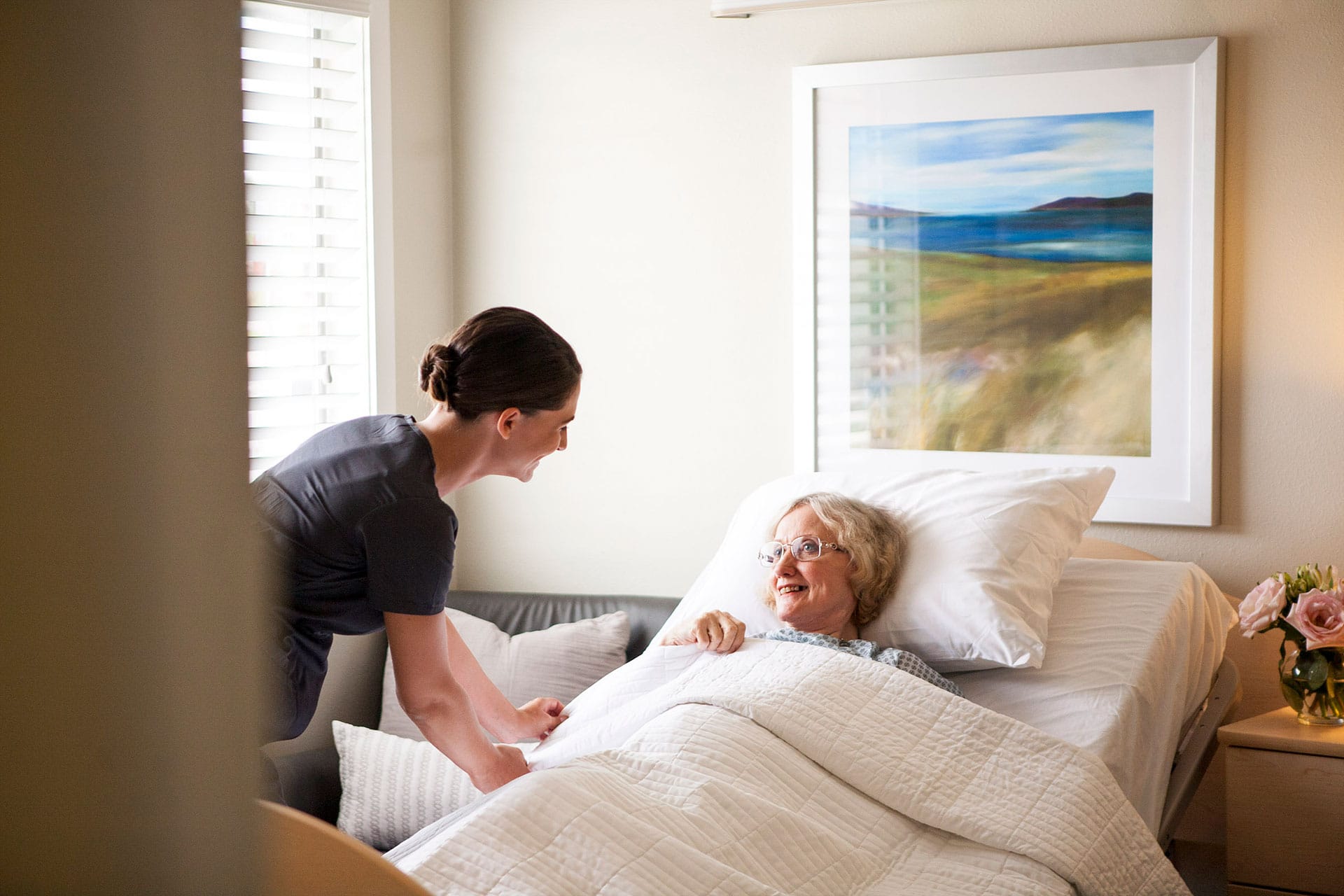 female nurse smiling while tucking patient into bed