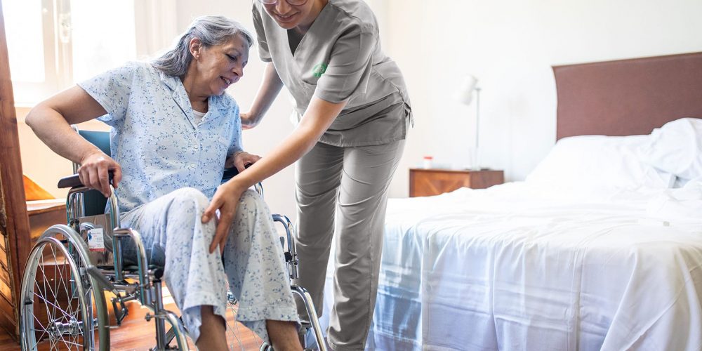 Registered Nurse helping elder woman in bed from their wheelchair
