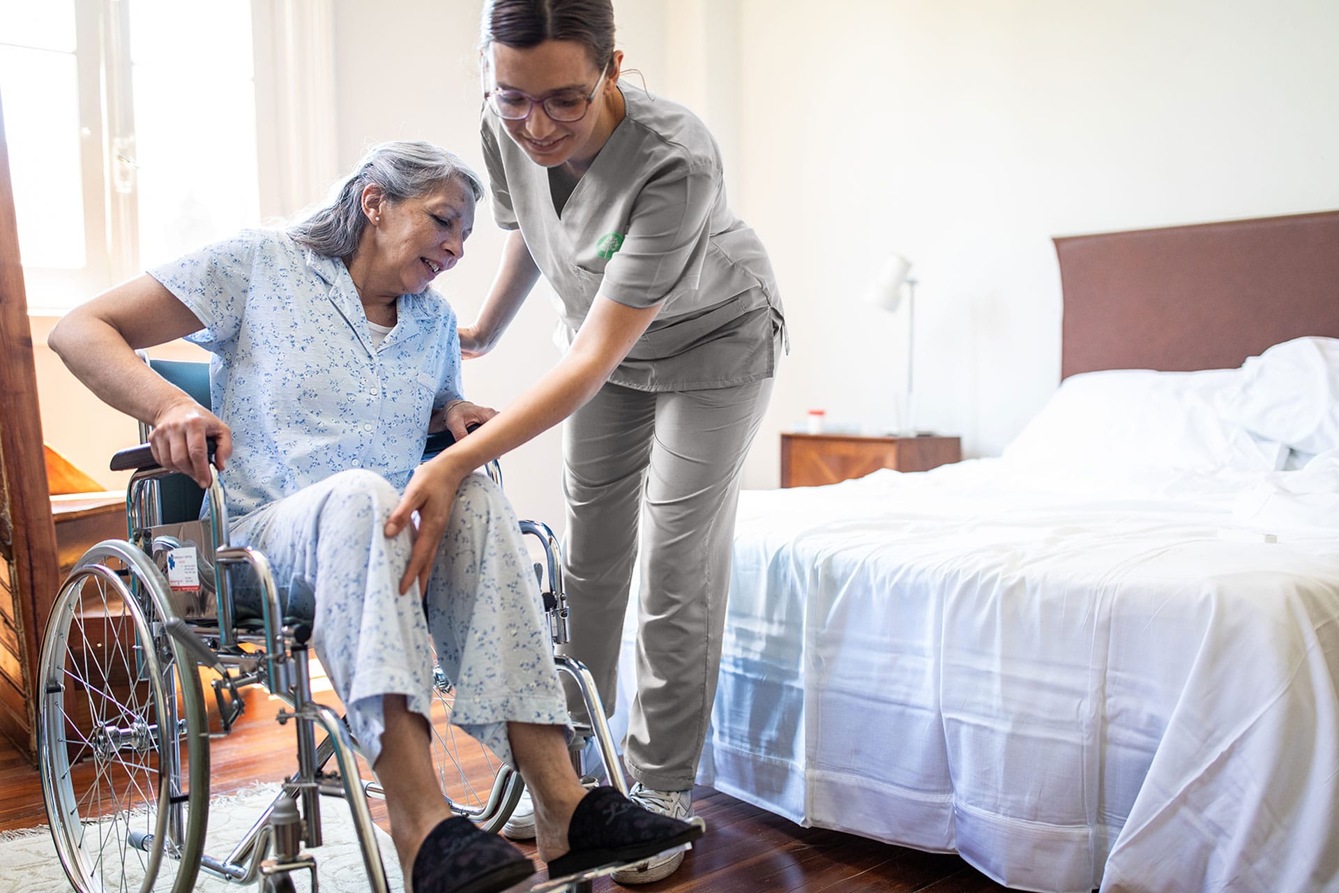 Registered Nurse helping elder woman in bed from their wheelchair