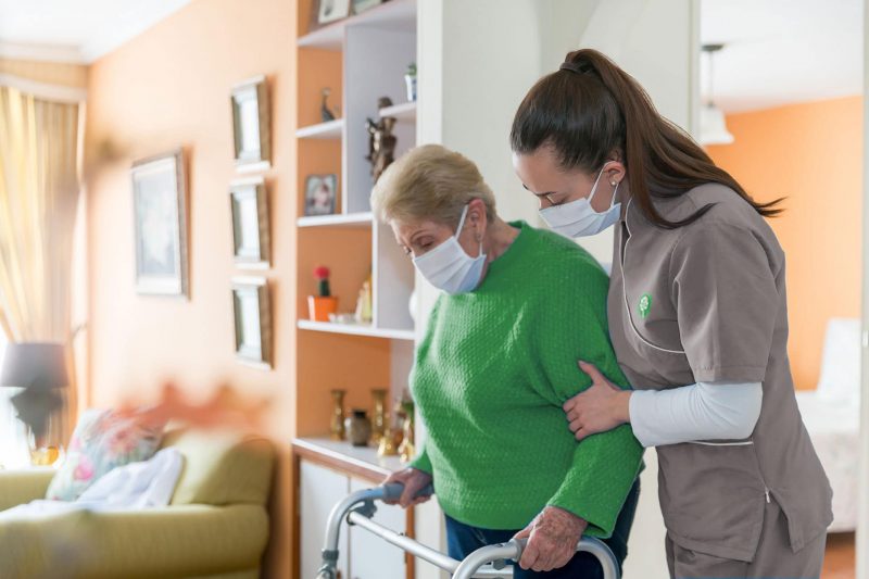 CNA (certified nursing assistant) helping an elderly patient walk with her walker