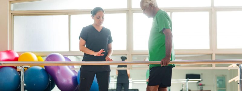 Skilled nurse helping male patient with physical therapy to walk