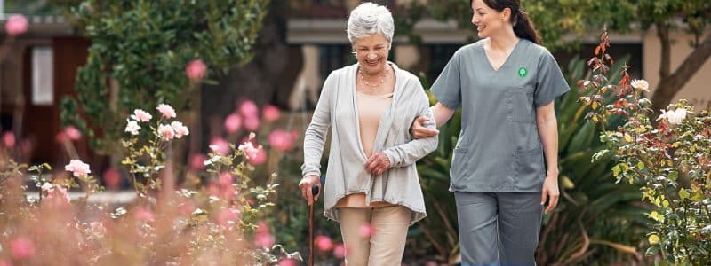 Elderly patient happily walking with a cane with a skilled nurse