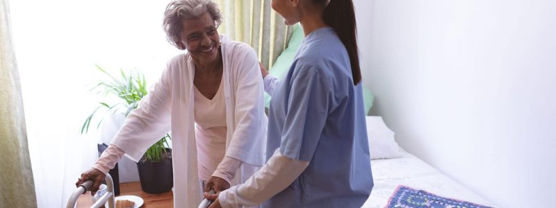 registered nurse helping elder woman out of bed with assistance of her walker