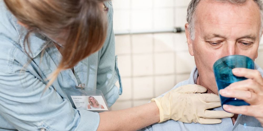 Skilled nurse examining a patient's neck and helping to drink water