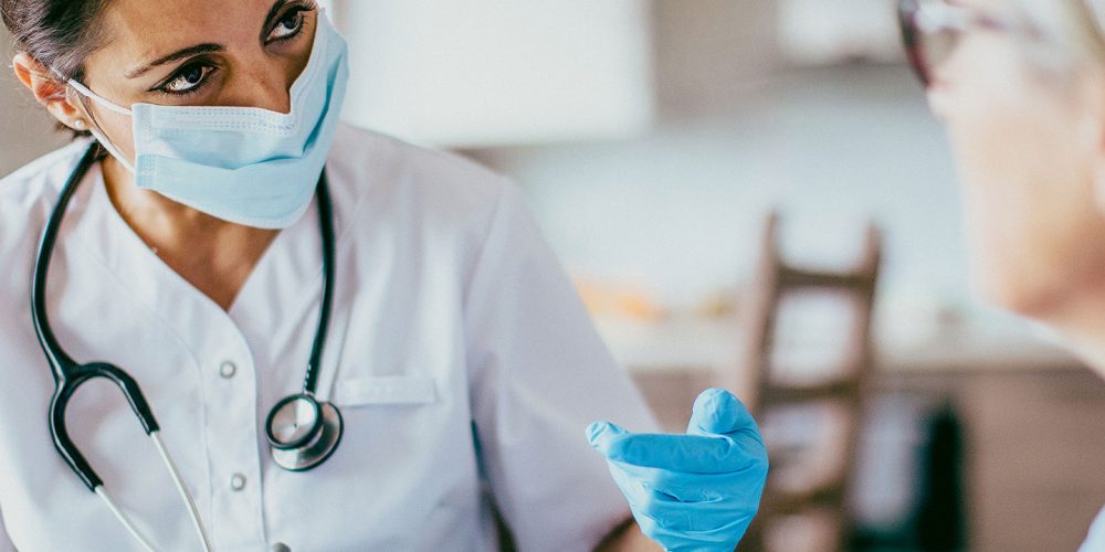 Skilled nurse with mask talking to a patient