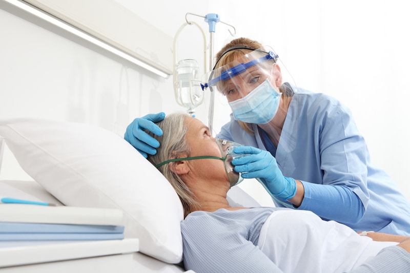 Skilled nurse puts oxygen mask on respiratory care patient in bed