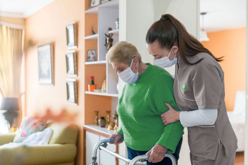 certified nurse helping elderly patient walk with walker