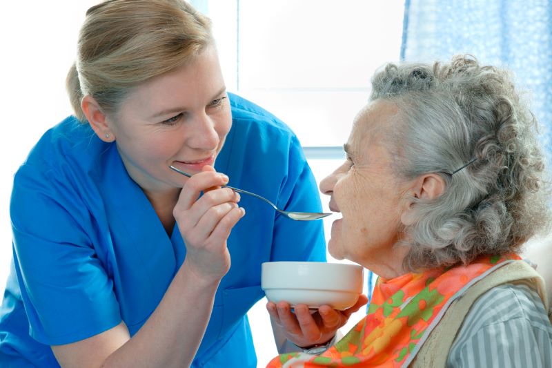 certified nurse helping elderly patient eat soup