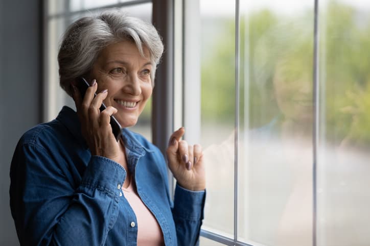 Older woman standing near window talking on smartphone