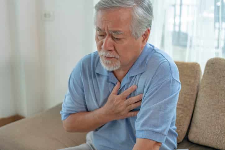 Older man sitting down holding heart in mild pain