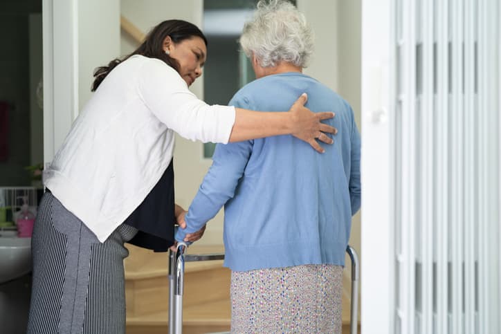 Caregiver helps elderly old woman walk with walker