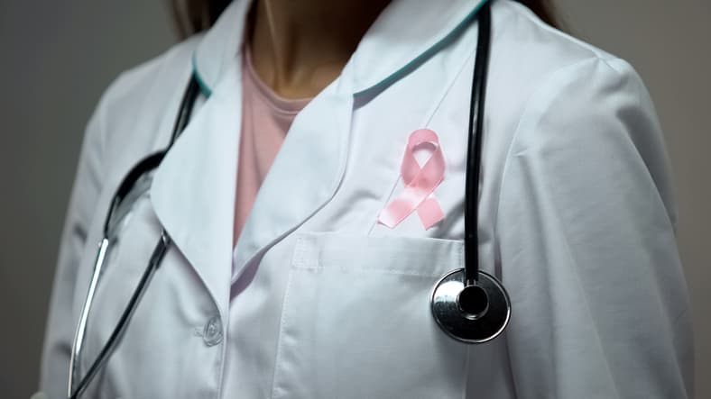 doctor attaching pink ribbon to white medical suit