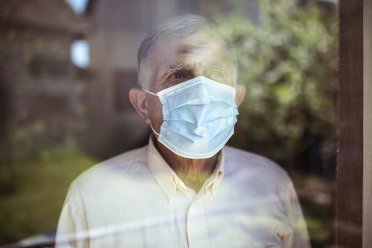 Older man wearing facemask looking out window