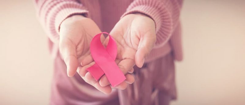 Woman holding pink ribbon in hands for breast cancer awareness