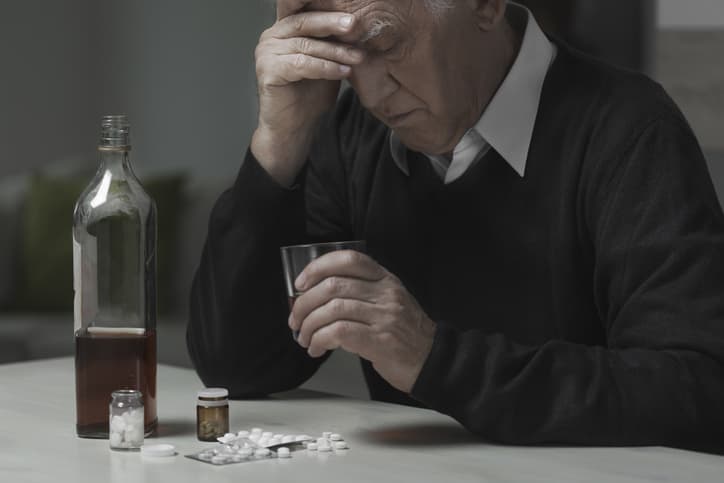 elderly man drinking with pills on table