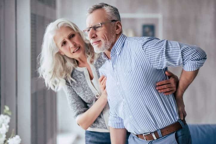 older man at home in pain with his wife