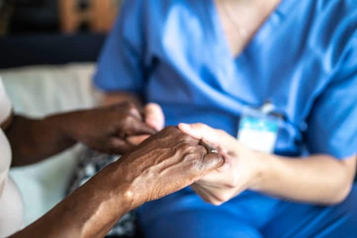 A nurse holding the hands and comforting a patient with mixed dementia.
