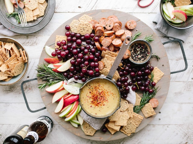 A charcuterie board featuring grapes, apples, cheese, crackers, seeds and meat.