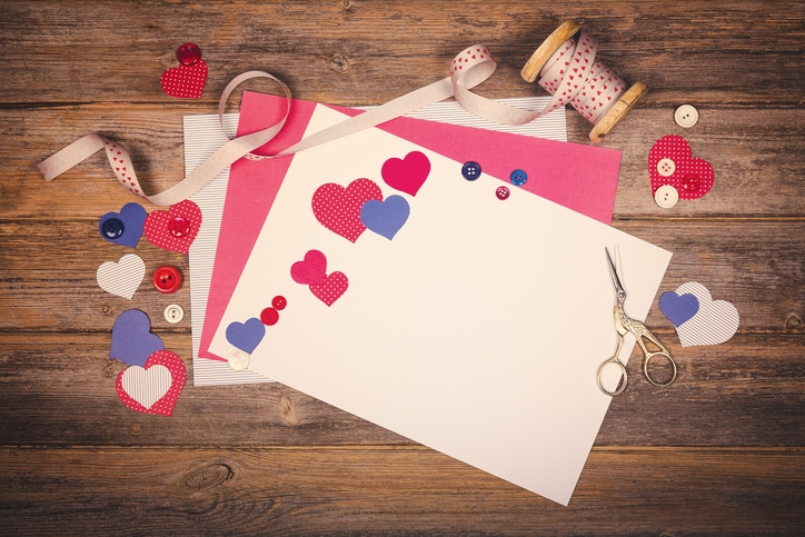 Construction Paper With Ribbon And Heart Shaped Cutouts Layering Over Both, Along With A Pair Of Scissors. 