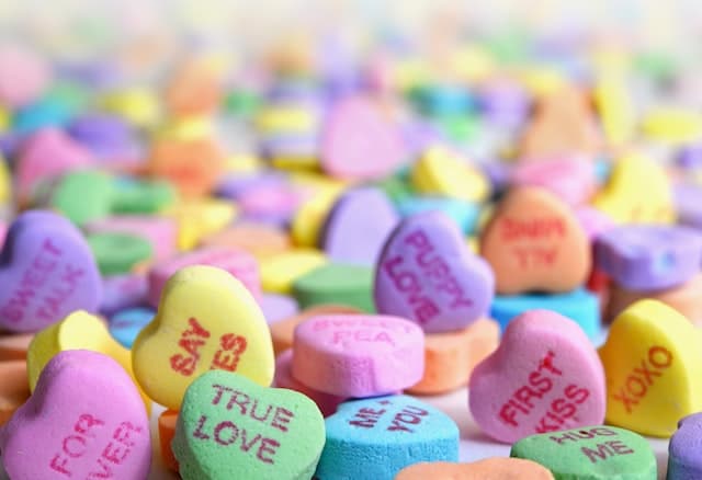 Assorted candy hearts with sayings written on them. The clearer ones saying: true love, forever, say yes, puppy love, me + you, first kiss and XOXO.