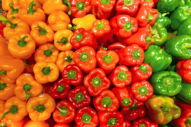 An Image Filled With Colored Peppers. From Left To Right: Orange Peppers, Red Peppers, Green Peppers.