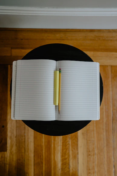 A blank lined notebook opened to its center with a pencil and highlighter in the spine.