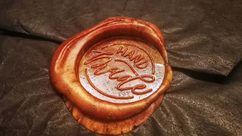 An orangish-brown wax seal with the words "handmade" stamped into its center. 