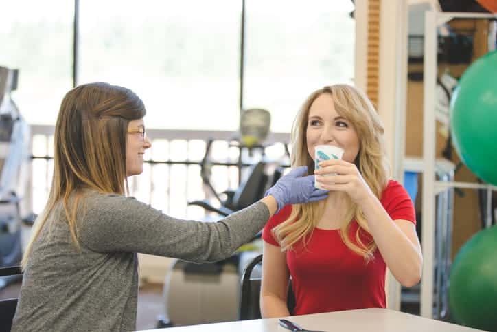 A female speech therapist is helping a young adult female patient inside of a clinic.