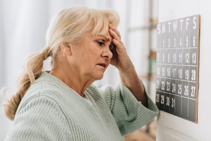 an elderly woman looking at the calendar, trying to remember.
