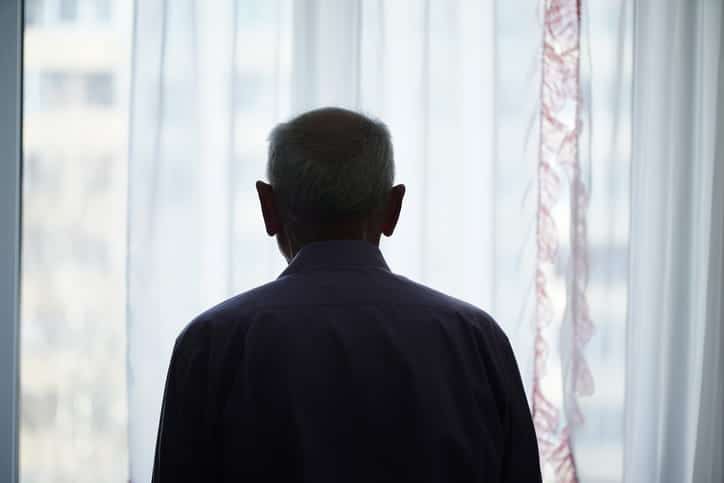 A silhouette of an elderly man staring out the window.