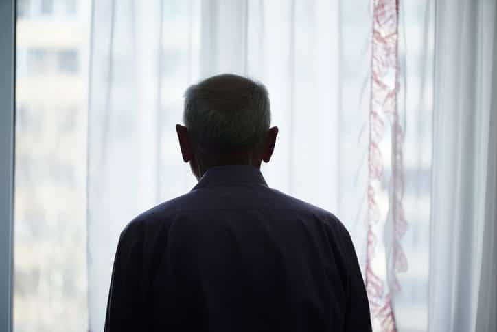 A Silhouette Of An Elderly Man Staring Out The Window.