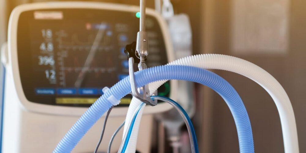 A close up of ventilator tubes, with the machine in the background.