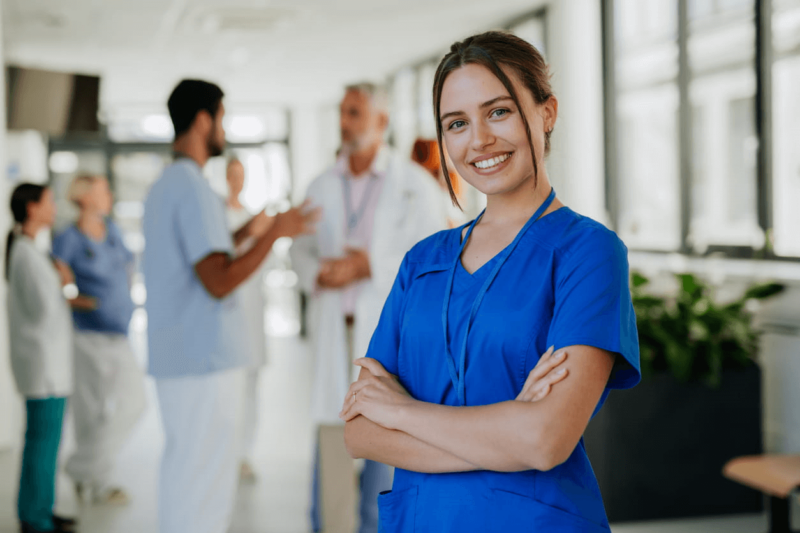 A nurse in blue scrubs smiling at a skilled nursing facility.