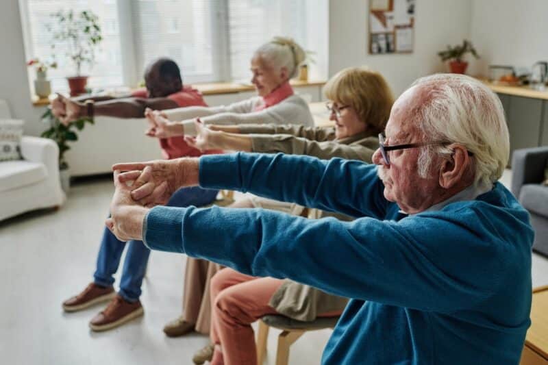 Four seniors doing stretching exercises with their arms while sitting down.