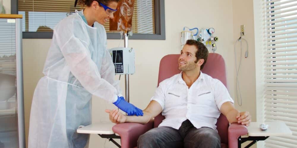 A nurse setting up specialty infusion for her patient as he sits in a chair.