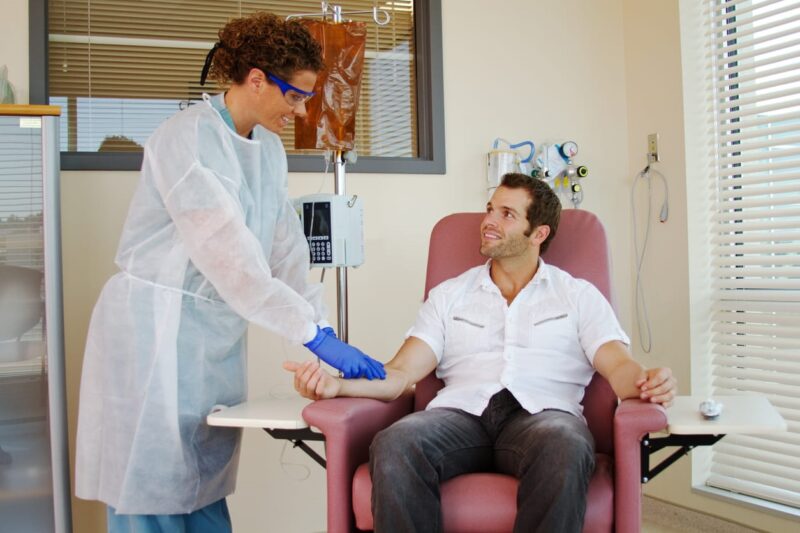 A nurse setting up specialty infusion for her patient as he sits in a chair.