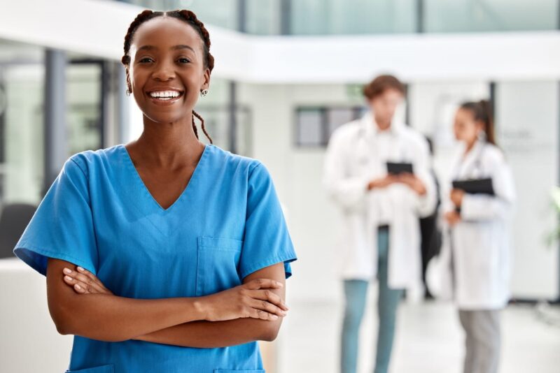 A nurse in blue scrubs at a skilled nursing facility, smiling with her arms crossed.