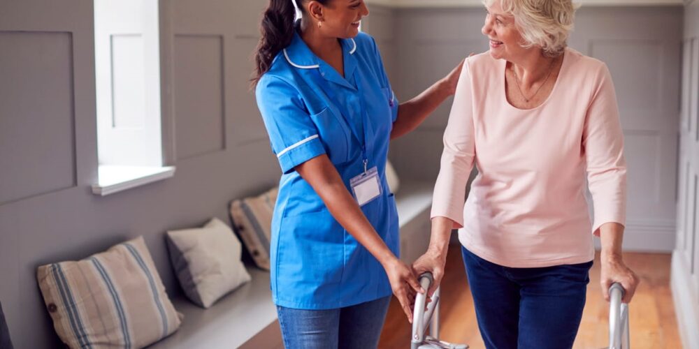 An aid assisting an elderly woman with a walker at a skilled nursing facility.