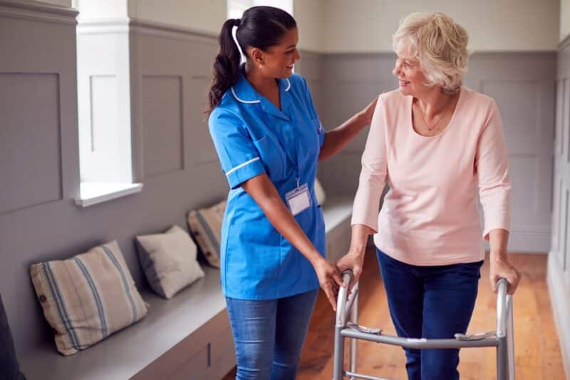 An aid assisting an elderly woman with a walker at a skilled nursing facility. 