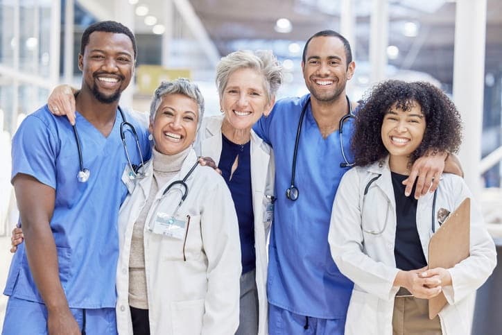 Five doctors and nurses lined up in a row, smiling together at a skilled nursing facility.