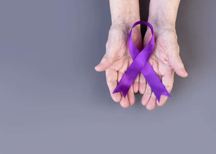 A hand holding a purple ribbon to raise Alzheimer's awareness.