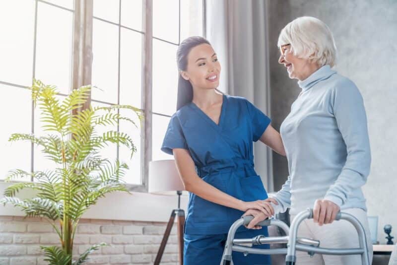 A nurse assisting an elderly woman with a walker at a skilled nursing facility.
