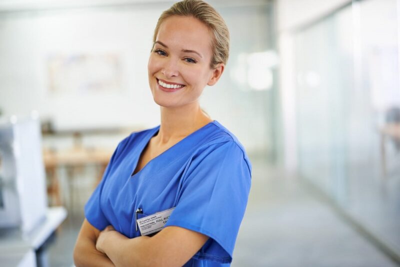 A nurse in blue scrubs smiling at a skilled nursing facility.