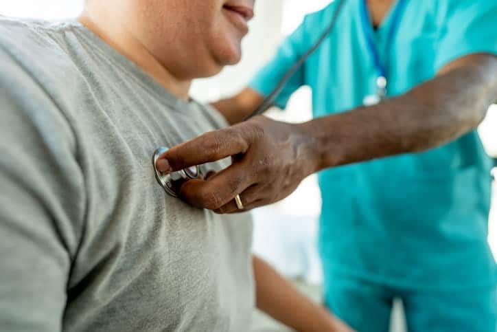 A doctor listening to an individual's heartbeat with a stethoscope during his yearly checkup. 