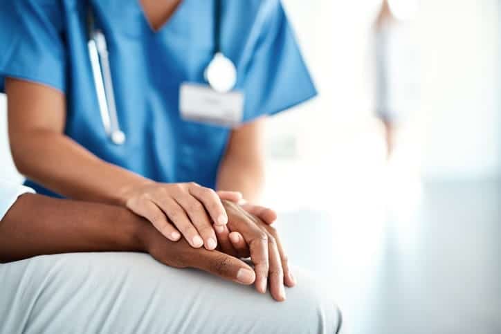 A nurse holding the hand of a patient within an assisted living facility. 