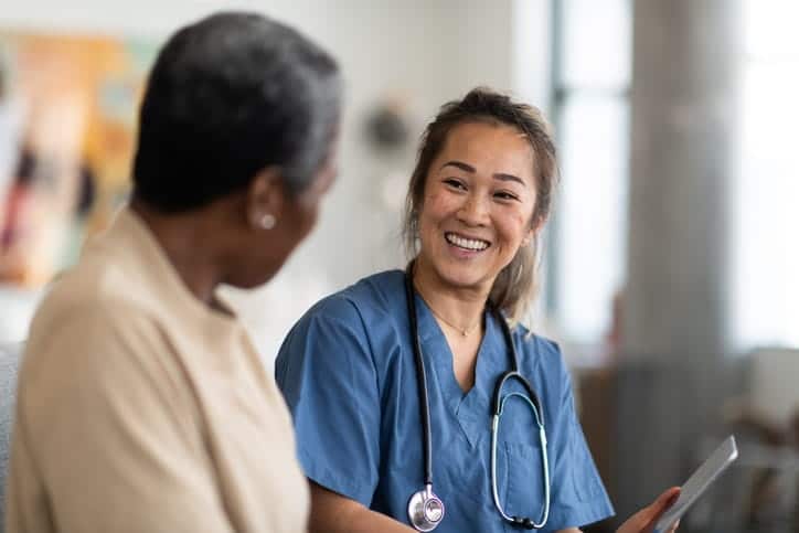 A nurse is talking to and smiling with an elderly patient at a skilled nursing facility. 