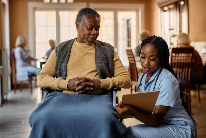 A nurse speaking with a patient at assisted living facility. She's holding a clipboard.