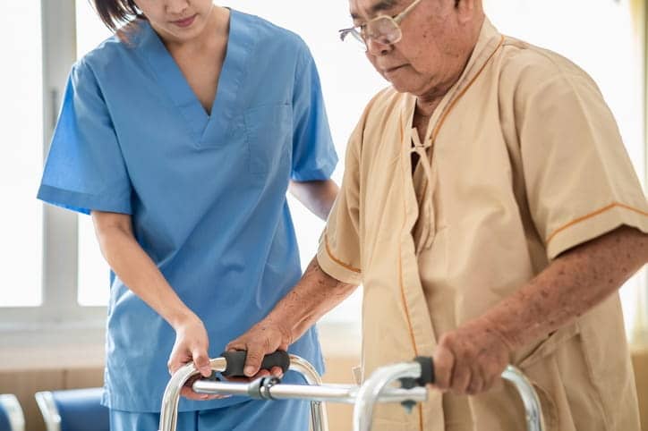 An aid assisting an elderly man with a walker after he suffered a stroke. 