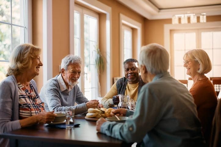 Five elderly people are eating breakfast together at an assisted living facility. 