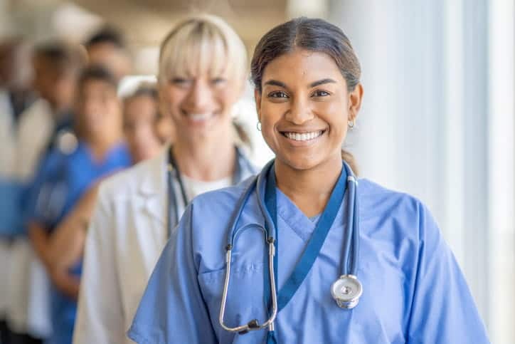 Focus is on a line of medical professionals smiling at the camera. The first nurse is smiling and the camera goes out of focus the further back the line goes. 